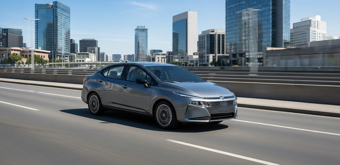 Automóvil sedán Nissan Versa gris en movimiento sobre un puente con edificios al fondo.