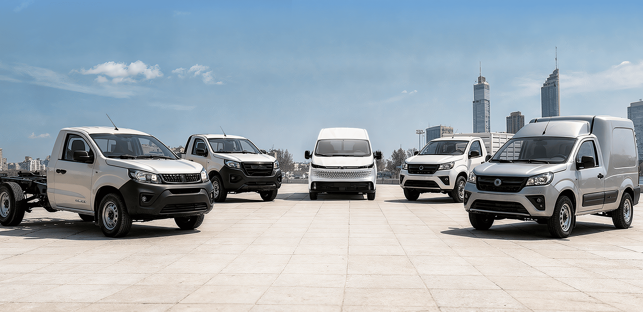 Flotilla variada de vehículos comerciales blancos, incluyendo camionetas de carga tipo van y pick-ups, ordenados en una plaza con edificios al fondo.