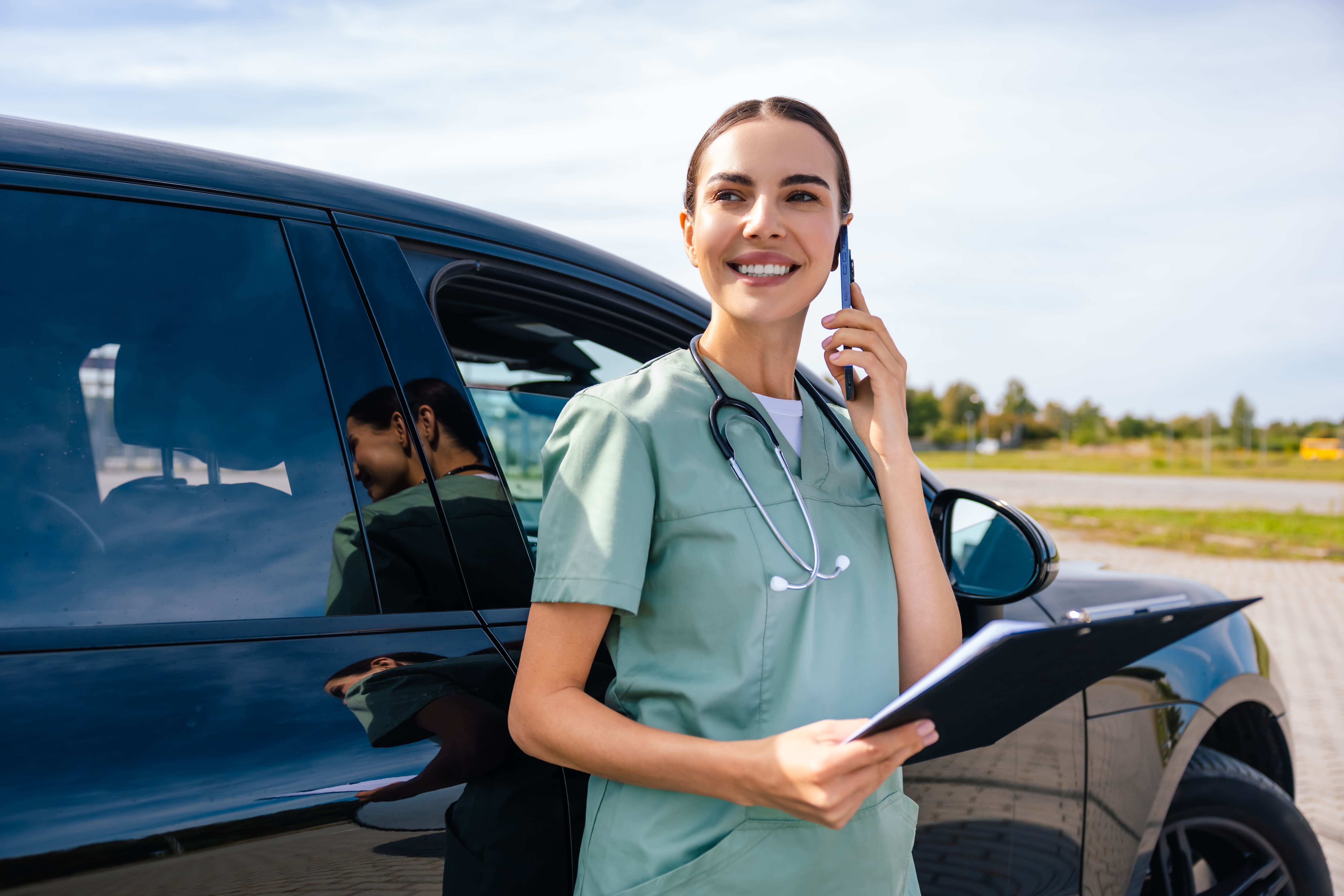 Profesional de la salud con uniforme quirúrgico habla por teléfono junto a una camioneta oscura estacionada.